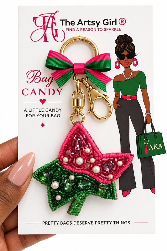 A hand holds a white retail card featuring a Ivy leaf beaded bag charm keychain. The card shows the brand name 'The Artsy Girl' and the product name 'Bag Candy'.