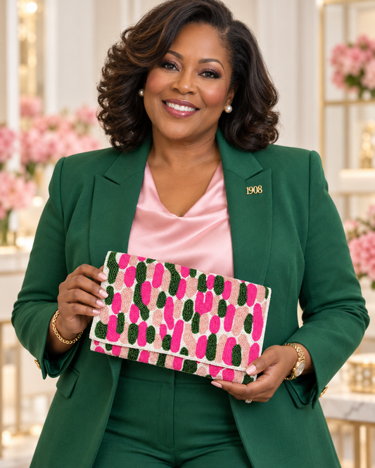 A woman wearing a green blazer and matching pants over a pink satin top, holding a patterned clutch bag with pink, green, and beige brushstroke motifs.