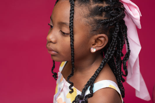 Little girl with a pink bow in her hair wearing heart glitter earrings.