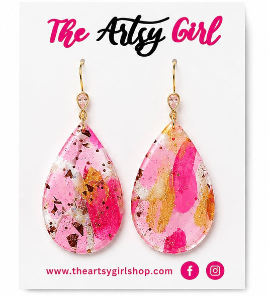 Teardrop-shaped earrings with pink and gold design on a 'The Artsy Girl' branded card.