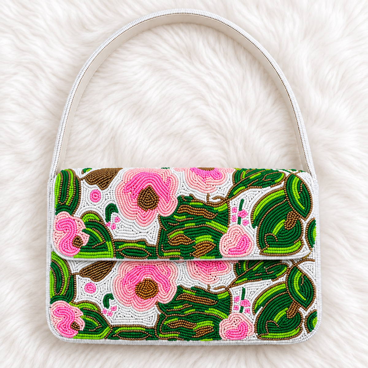 A small structured handbag with a white handle and body, covered in a colorful beaded floral pattern of pink flowers and green leaves on a white background, laid flat on a white faux fur surface.
