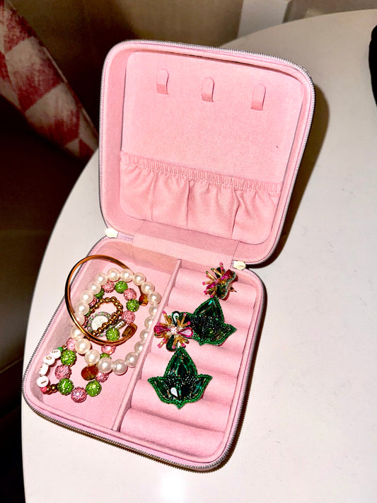 Pink jewelry case with green and pink jewelry on a white surface