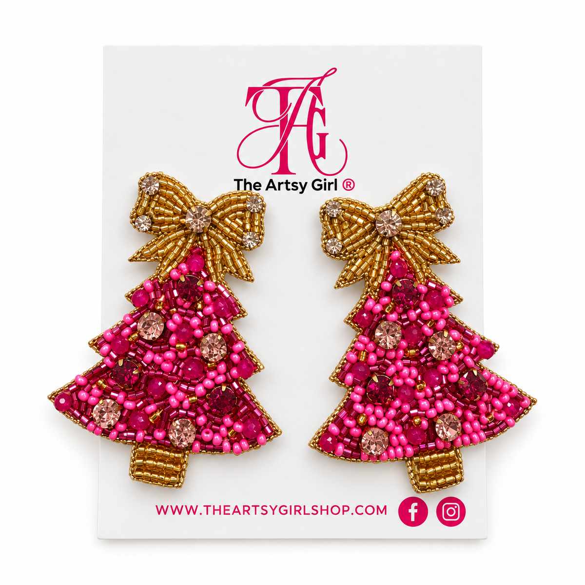 A pair of Christmas tree-shaped beaded earrings by The Artsy Girl, featuring bright pink seed beads and gold beaded borders with rhinestone accents, displayed on a white branded backing card.