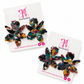 Two pairs of flower-shaped earrings with a marbled tortoiseshell pattern in navy, teal, magenta, and yellow, displayed on white cards with pink branding for 'The Artsy Girl'.