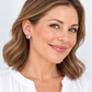 A close-up portrait of a woman with brown hair wearing a small round stud earring with a colorful, iridescent, flower-like design. She is smiling and wearing a white top against a clean, light background.