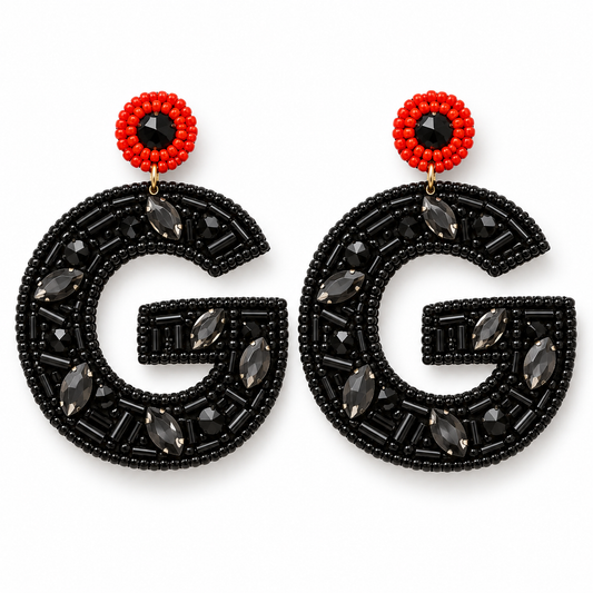 A pair of statement earrings featuring a large black beaded letter 'G' adorned with dark gray faceted marquise and oval crystals, topped with a red beaded circle and a central black faceted gemstone.