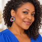 A close-up portrait of a woman with curly dark hair wearing a bright blue top and a colorful, teardrop-shaped earring covered in small multicolored sequins.