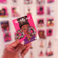 A pair of multicolored glittery earrings displayed on a pink card, with the text 'The Artsy Girl' and 'Glitz Therapy' on the earrings' description.