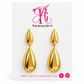 A pair of gold teardrop drop earrings displayed on a white branded card that reads 'The Artsy Girl' with the website and social icons below.