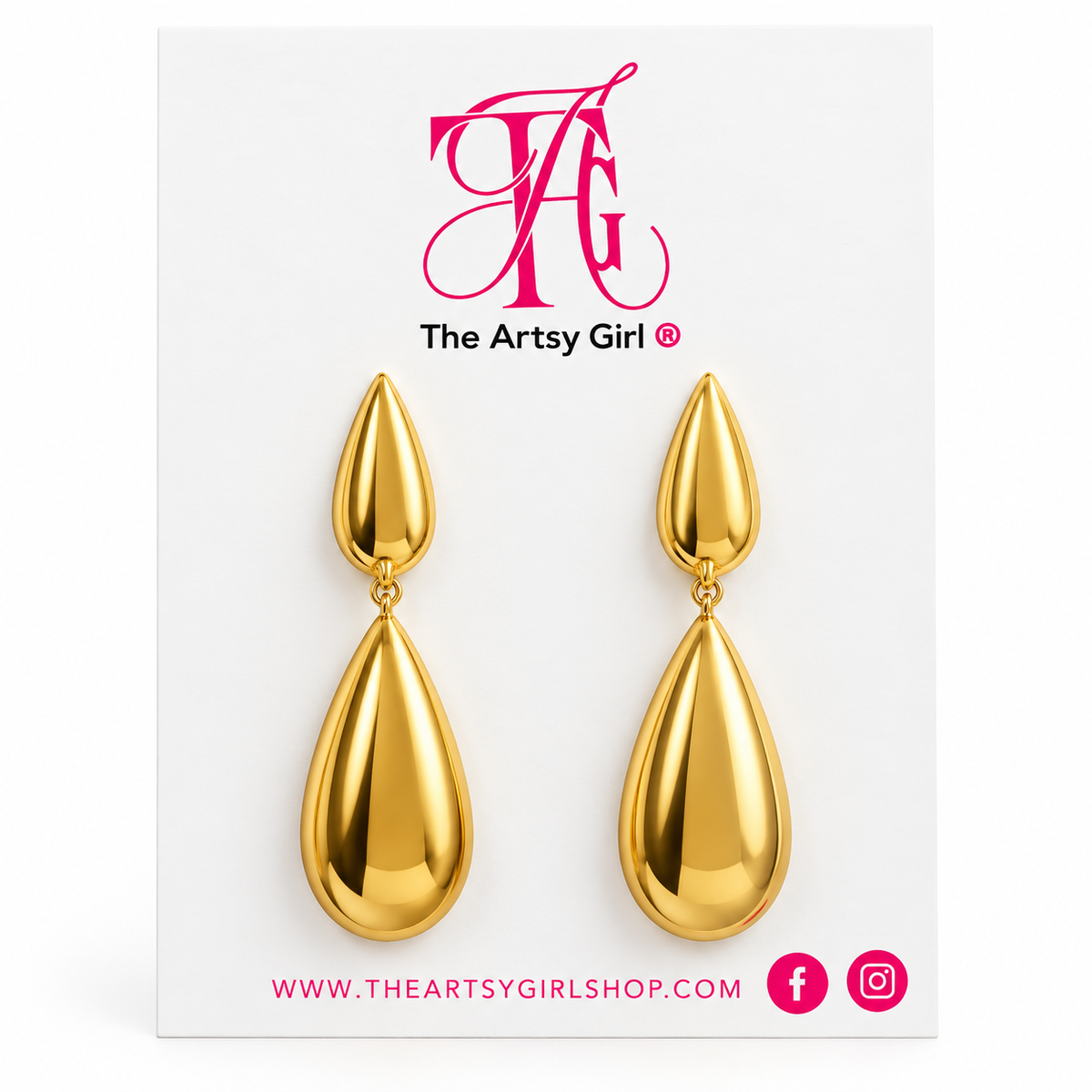 A pair of gold teardrop drop earrings displayed on a white branded card that reads 'The Artsy Girl' with the website and social icons below.