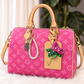 A pink Louis Vuitton monogram handbag with tan leather handles and a pearl keychain charm, displayed on a white faux fur surface with a blurred green plant in the background.