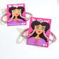 A pair of pink 'Hey Glitter, Hey' hoop earrings with glitter embellishments, displayed on a branded card.