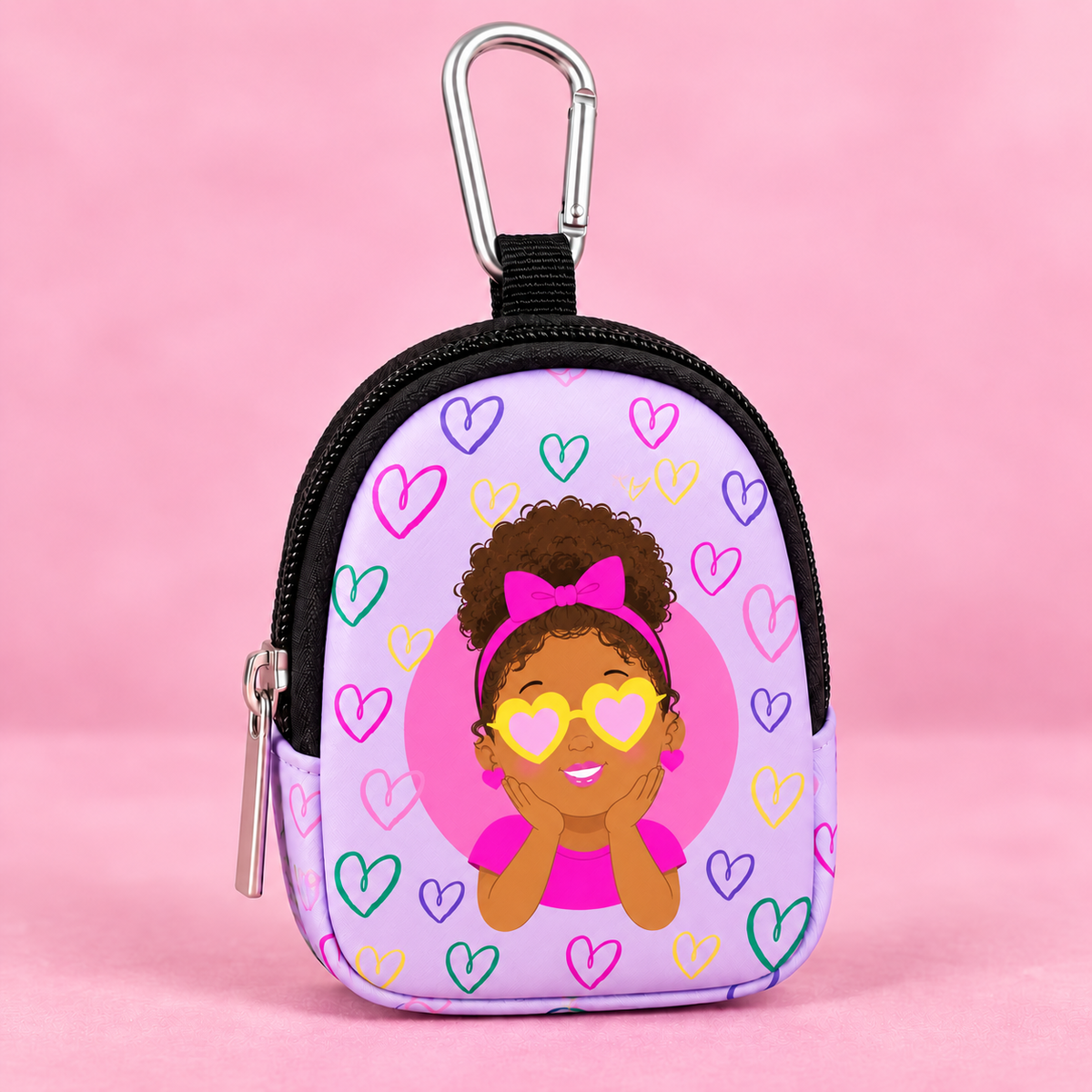 A small zippered coin purse with a carabiner clip, featuring a cartoon girl with heart-shaped sunglasses and colorful heart patterns on a light purple background, set against a solid pink backdrop.