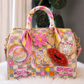 A highly decorated, patchwork-style handbag with pink and gold checkered patterns, embellished with a pink satin scarf, a pink flower applique, a red sequined lip bag charm, and various text patches including 'Queen', 'Superstar', and 'Be Lovely'.