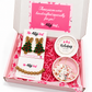 An open pink gift box from The Artsy Girl containing handmade holiday-themed jewelry and candle melts. The box is lined with pink paper and features a pink insert card.