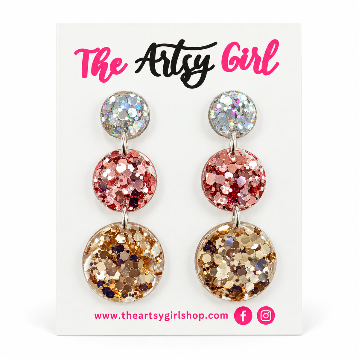 A pair of triple-stone dangle earrings with holographic, pink, and gold glitter discs on silver posts, displayed on a white card labeled 'The Artsy Girl'.