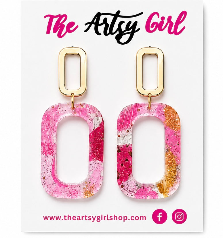 Pink and gold earrings on a card with 'The Artsy Girl' branding.