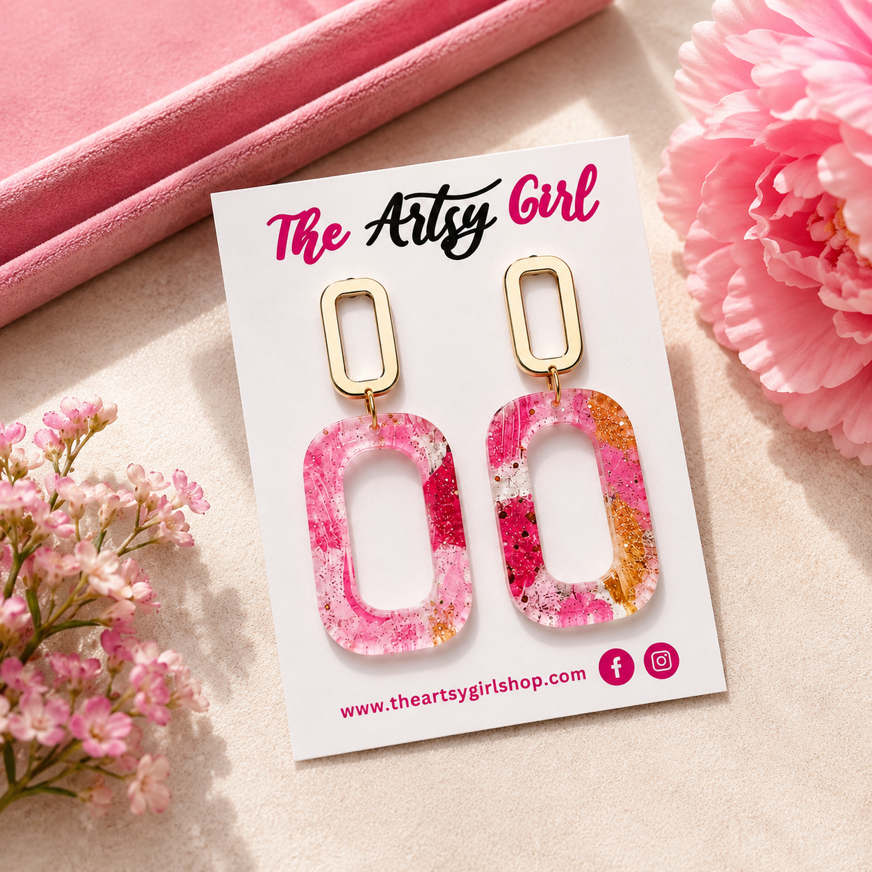 Pink and gold earrings on a 'The Artsy Girl' branded card with pink flowers around.