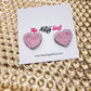 Heart-shaped pink earrings on a card with 'The Artsy Girl' branding on a textured gold background.