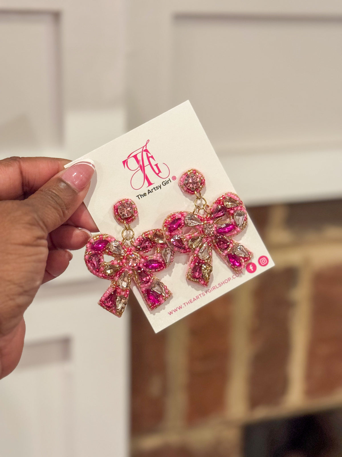 A pair of pink and gold bow-shaped earrings with crystal-clear stones, displayed on a card.