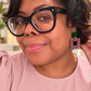 Woman in a blush outfit wearing emerald green studs with pink, green, and gold glitter square-frame earrings.