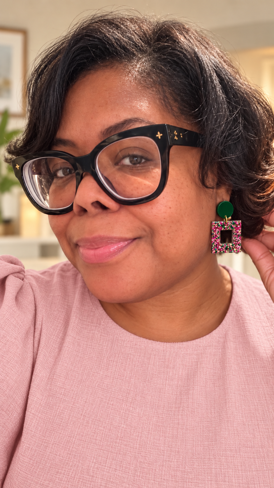 Woman in a blush outfit wearing emerald green studs with pink, green, and gold glitter square-frame earrings.