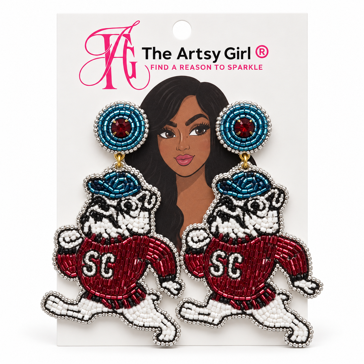 A pair of beaded dangle earrings featuring two bulldogs wearing red and white 'SCSU’ jerseys, hanging from blue and burgundy beaded circles. The earrings are displayed on a white backing card with a pink 'The Artsy Girl' logo and an illustration of a woman.