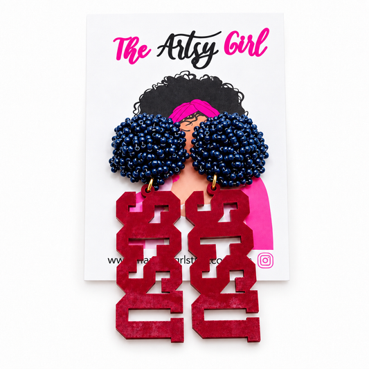 A pair of statement earrings displayed on a white backing card. The earrings feature two large, dark blue beaded pom-pom tops with gold-tone hooks, and long, chunky garnet letters spelling 'SCSU' below.