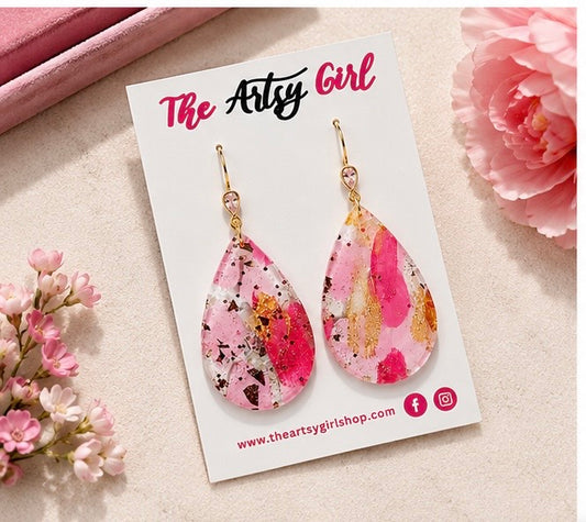 Pink and gold teardrop earrings on a 'The Artsy Girl' branded card with flowers around.