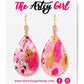 Teardrop-shaped earrings with pink and gold design on a 'The Artsy Girl' branded card.