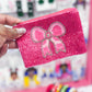 A hand holding a small, pink, beaded coin purse with a bow design.