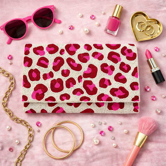 Hand-beaded pink and red spotted clutch purse styled in a chic flat lay with gold jewelry, lipstick, and pink accessories on a soft pink background.