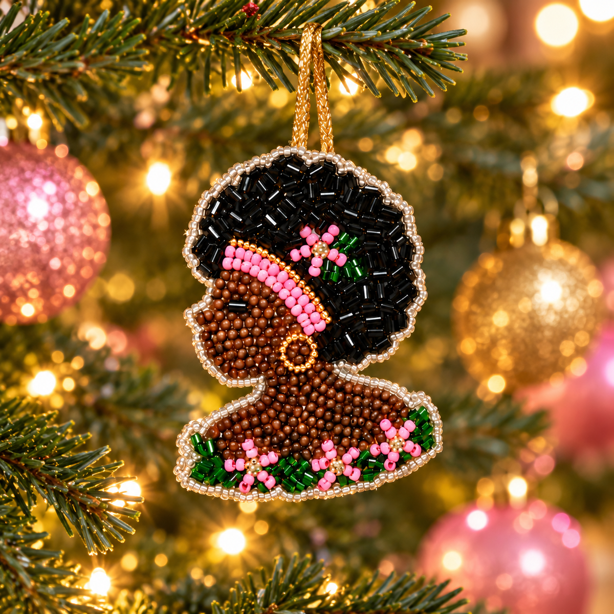 Beaded Black woman profile charm hanging on a Christmas tree decorated with pink and gold ornaments.