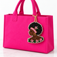 Beaded Black woman profile charm with a pink headband and floral details hanging from a solid hot pink tote.