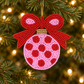 Pink and red beaded Christmas ornament with a large red bow hanging on an evergreen tree with warm white lights.