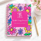 Floral Sparkle Energy Journal on a white desk beside a gold pen and pink flowers, with “Find a Reason to Sparkle” on the cover.