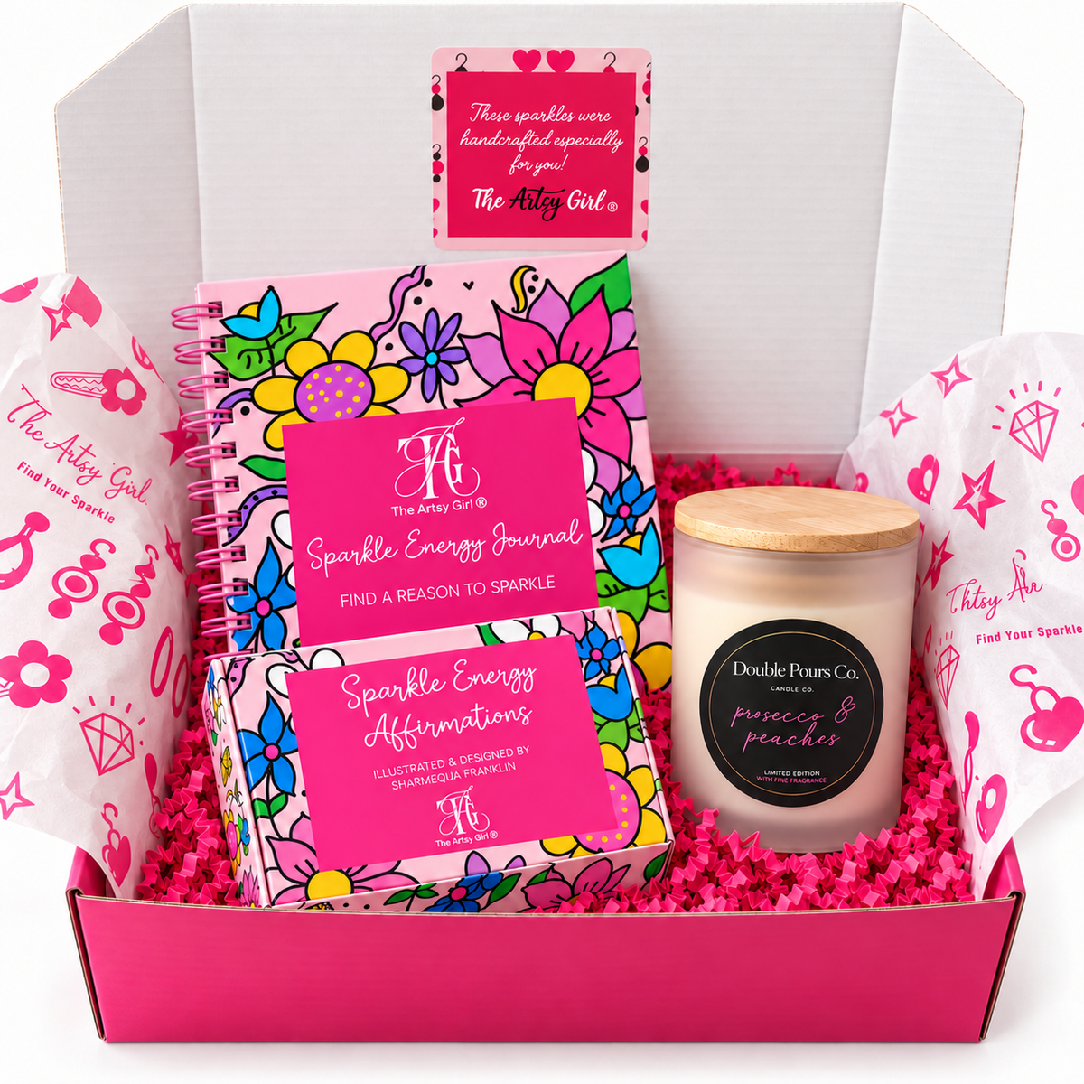 Open pink gift box containing a floral Sparkle Energy Journal, matching affirmation cards, and a Prosecco & Peaches candle.