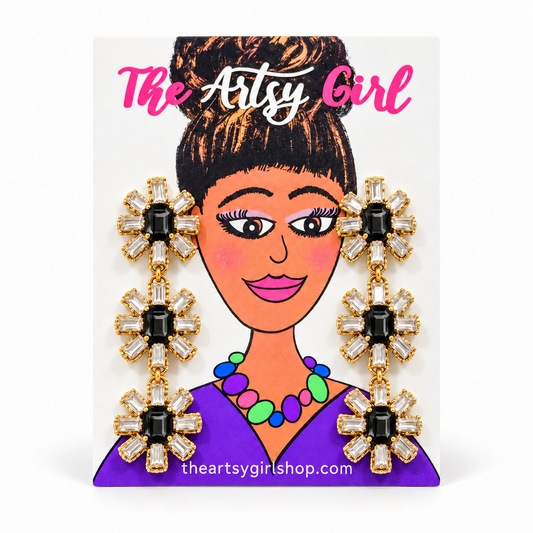 Three-tier floral earrings with black center stones, clear crystal petals, and gold settings on an Artsy Girl card.