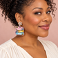Woman wearing “Black Girls Read” book-stack earrings with crystal flower tops against a blush background.