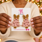 Woman holding The Artsy Girl card with blush pink beaded Christmas tree earrings featuring pink gemstones and gold bows.