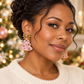 Woman wearing blush pink beaded Christmas tree earrings with pink gemstones and gold bows.