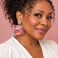 Woman wearing pink and orange “Book Club Girlie” book-stack earrings with crystal flower tops against a blush background.