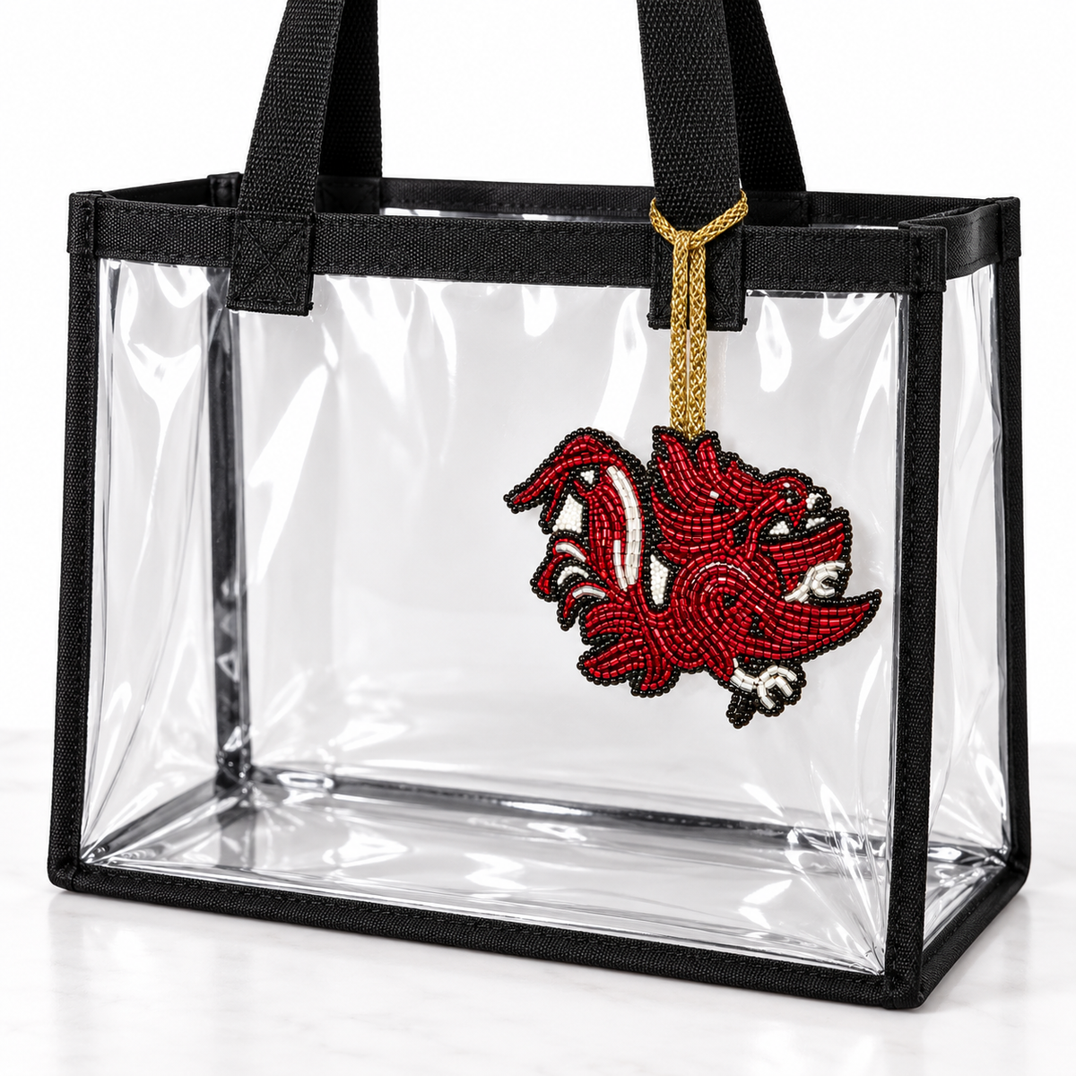 Garnet, black, and silver beaded Gamecock charm hanging from a clear game-day tote with black trim.