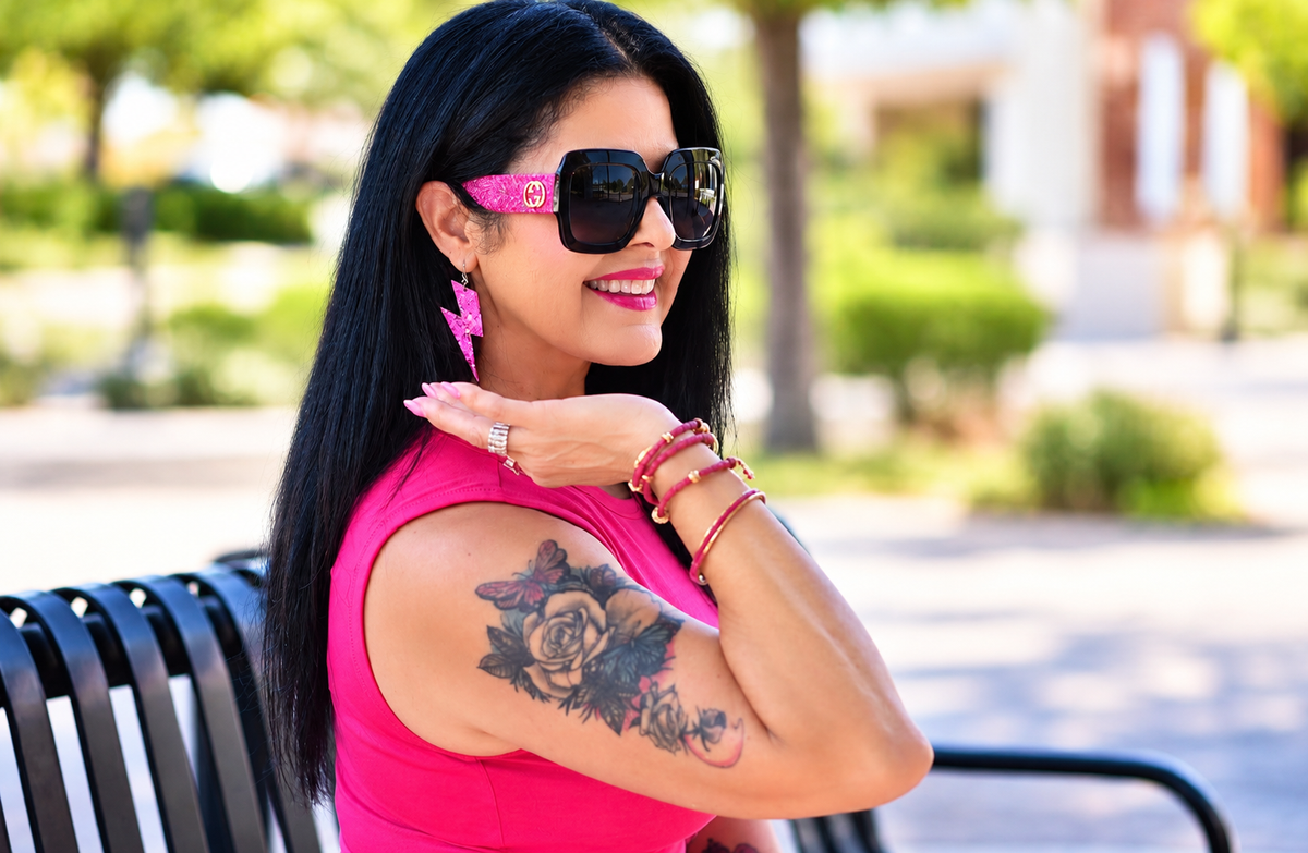 Woman in a pink sleeveless top and oversized sunglasses wearing pink glitter lightning bolt earrings outdoors.