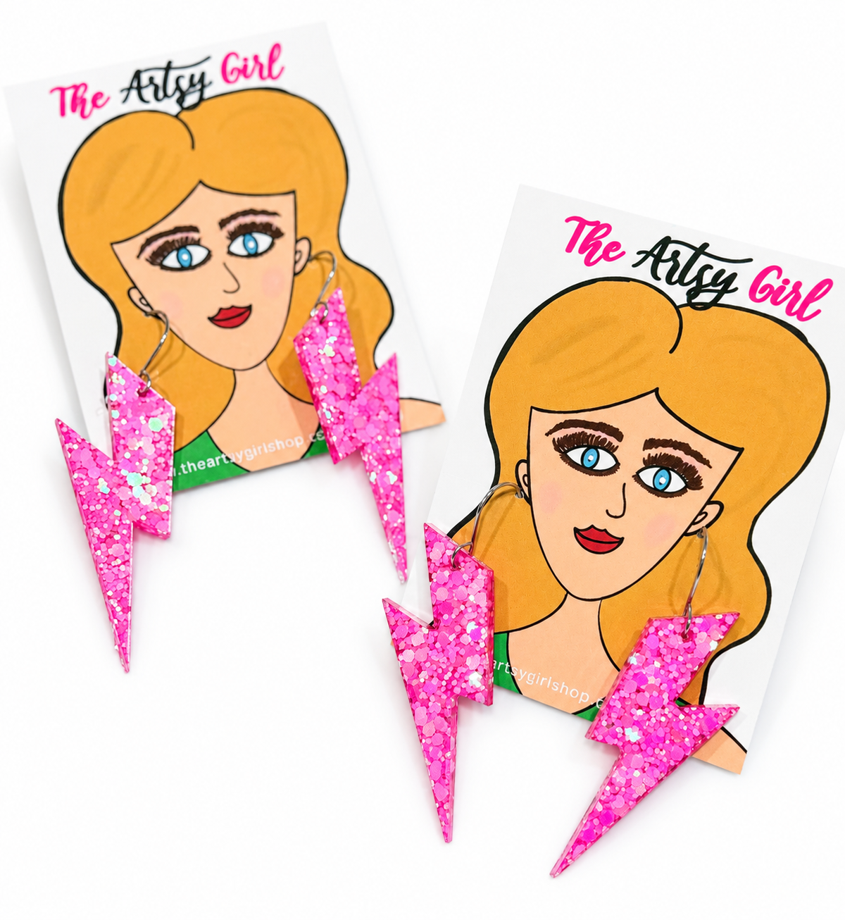 Pink glitter lightning bolt earrings displayed on two illustrated The Artsy Girl cards against a white background.