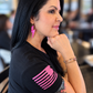 Woman in a black shirt wearing pink glitter lightning bolt earrings with her chin resting on her hand.
