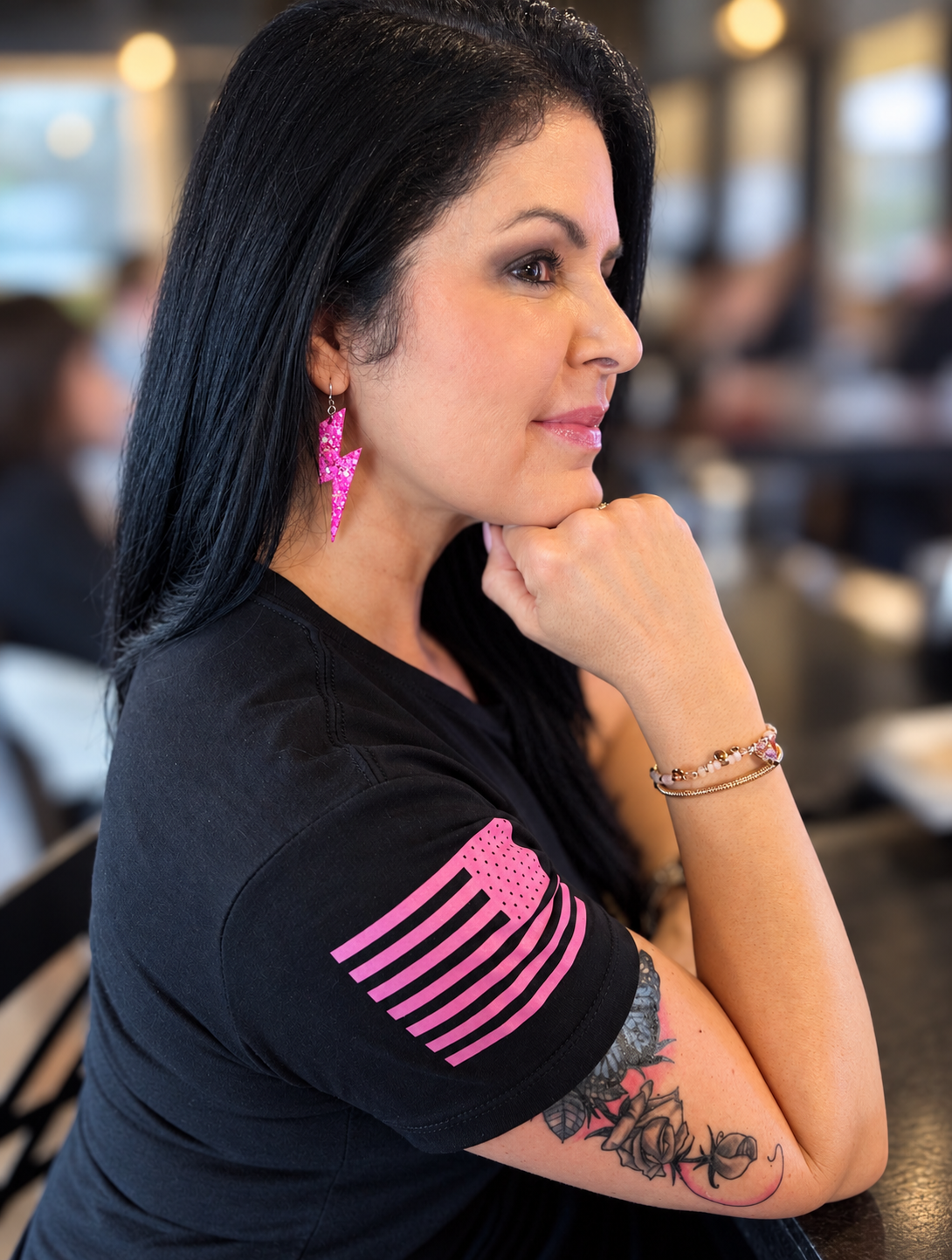 Woman in a black shirt wearing pink glitter lightning bolt earrings with her chin resting on her hand.