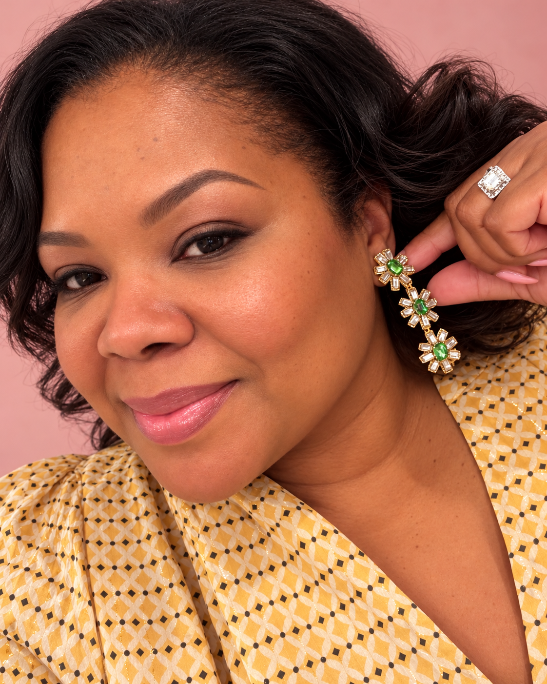 Woman wearing a yellow patterned top with floral earrings, indoors.