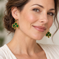 Woman in a cream blouse wearing gold hoops with green beaded three-leaf shamrock charms and gold edging.