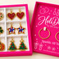 Open hot pink HoliDazzle box with six pairs of beaded holiday charms and one pair of gold hoops beside the divided tray.